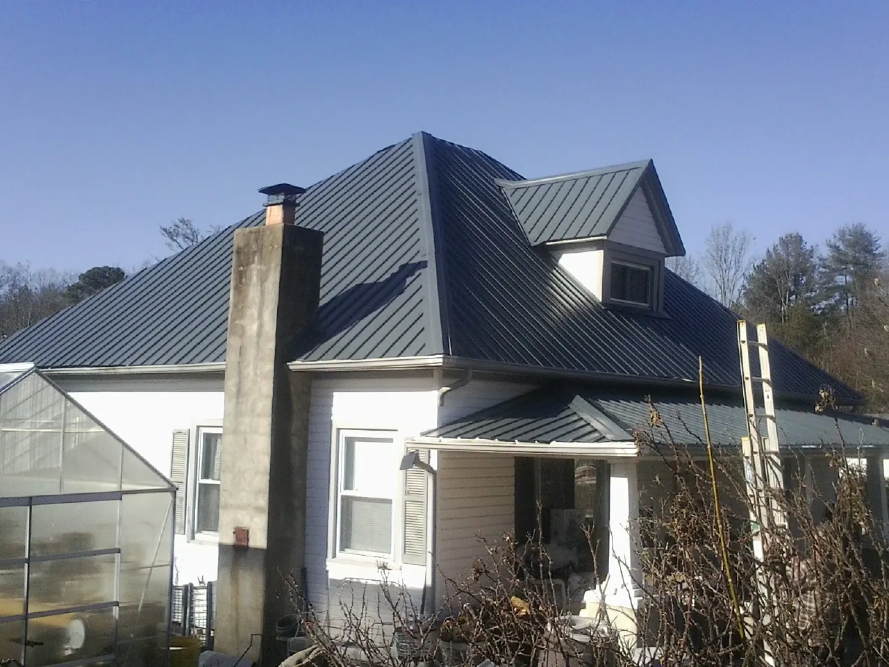 Dark blue standing seam metal roof on a white farmhouse with dormer — Slate & Tile Roof Repair by Roofing Brothers in Almira