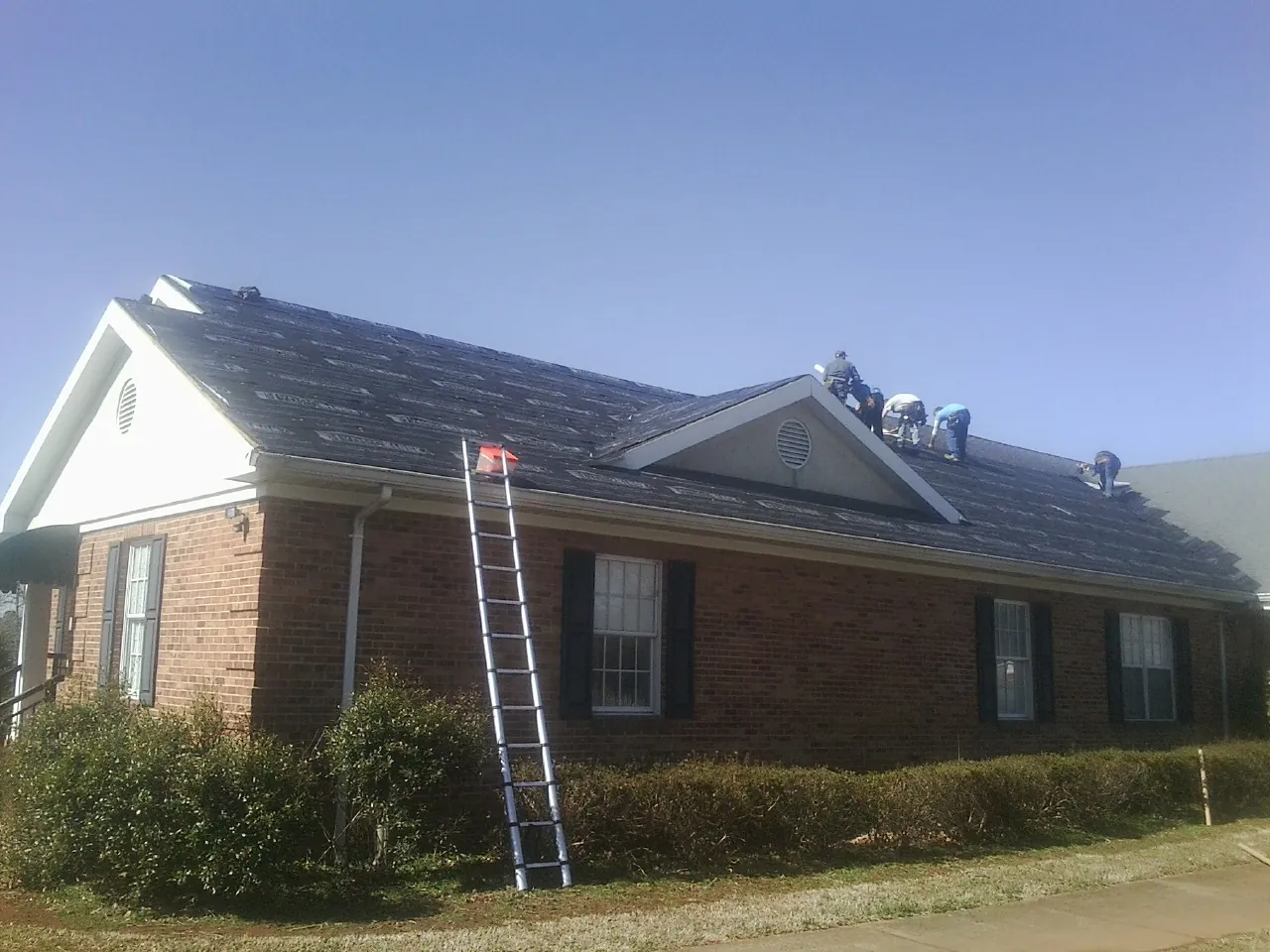 Crew tearing shingles off a brick ranch roof with a ladder set — Metal Roof Repair work by our crew in Almira