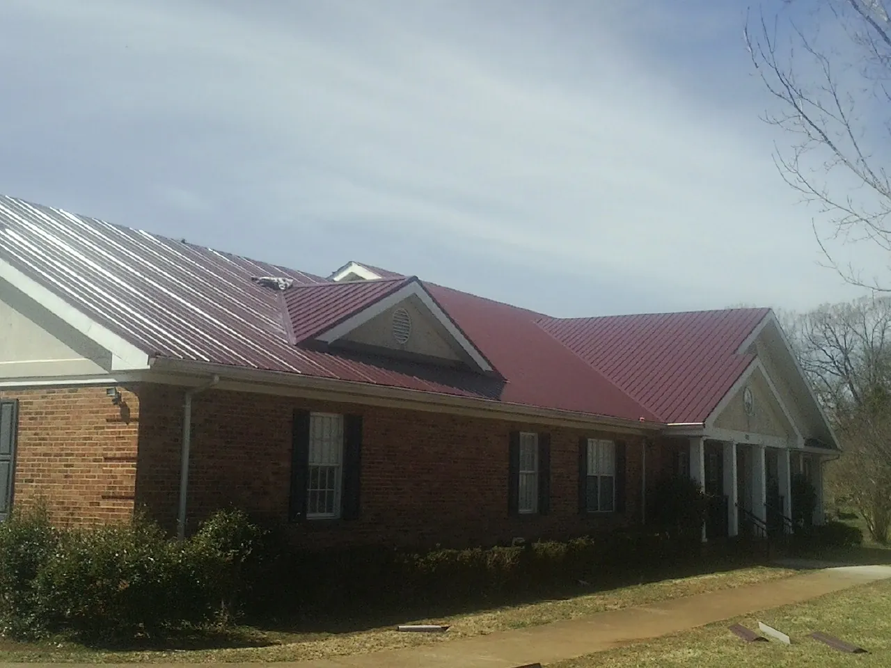 Red metal roof with gabled entries on a long brick building, from a Hail Damage Roof Repair job in Almira