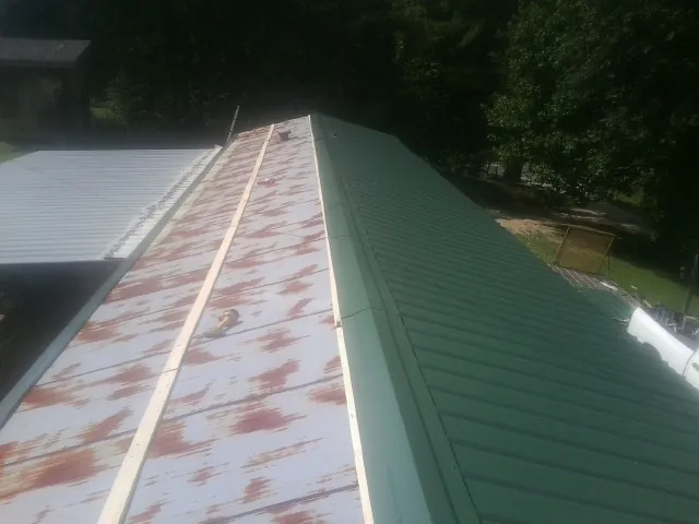 Old rusted panels beside newly installed green metal roofing — Wind Damage Roof Repair by Roofing Brothers in Almira