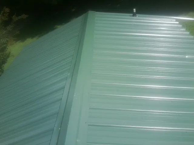 New green metal panels meeting at the ridge of a roof — Flat Roof Repair work by our crew in Almira