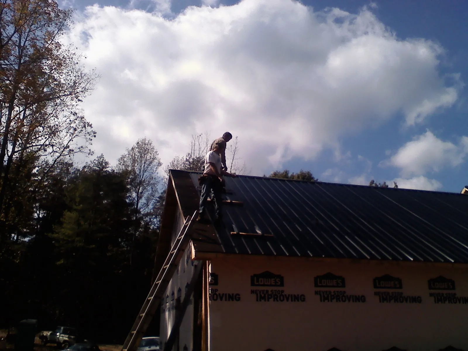 Roofer fastening dark metal panels high against a cloudy sky, from a Roof Inspection job in Almira