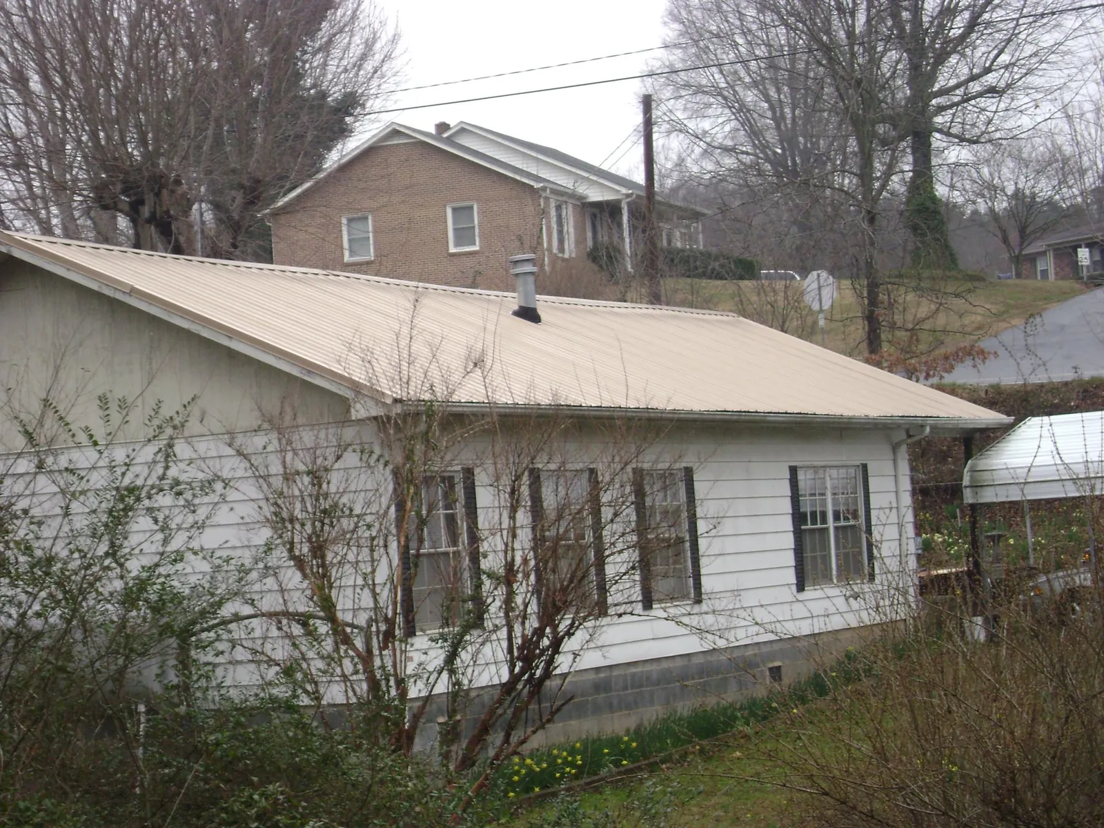 Tan metal roof on a white sided house set into a hillside — Commercial Roofing by Roofing Brothers in Almira